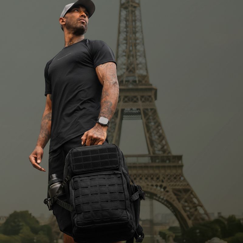 Homme tenant un sac militaire tactique noir avec système MOLLE devant la Tour Eiffel