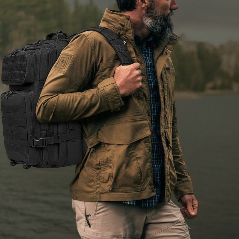 Homme en veste outdoor portant un sac militaire noir à sangles MOLLE près d’un lac