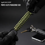 Gros plan détaillé du tressage de paracorde Vert OD d'un porte-clé, avec logo Militaire Faction discret, contre un fond flou d'équipement tactique.