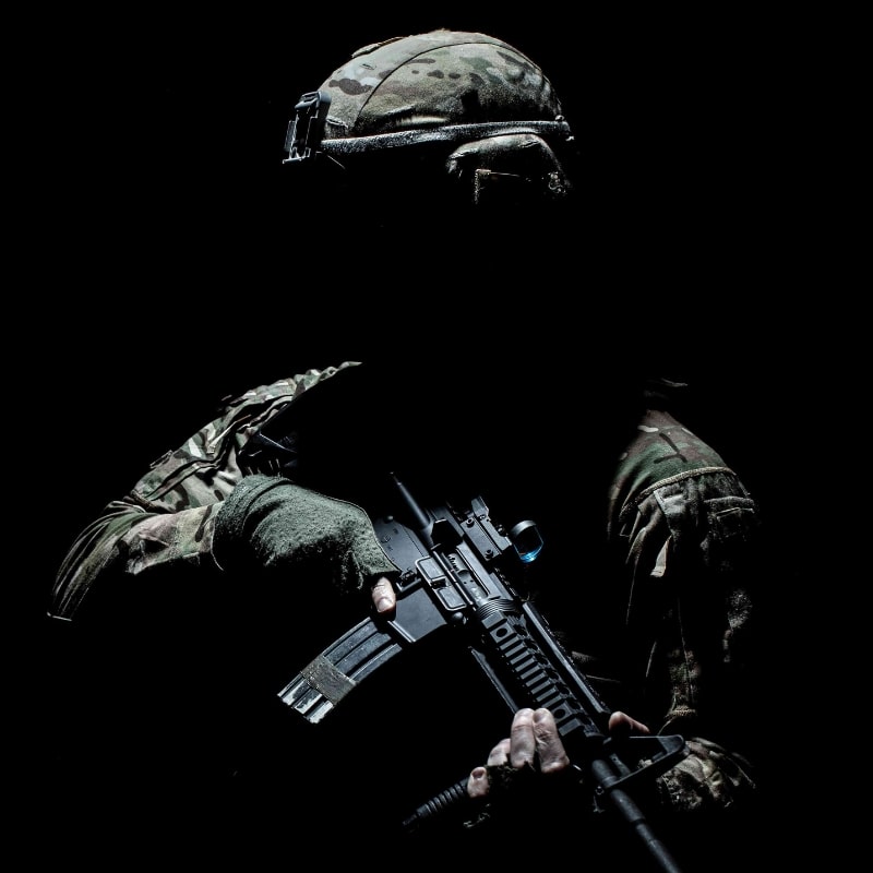 Soldat tactique camouflé tenant une arme d'assaut dans l'obscurité, équipé de gants, casque et tenue militaire – ambiance sombre, photo réaliste haute intensité.